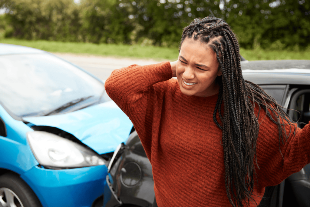 Black woman grabbing her neck with a blue car and a black car crashed behind her