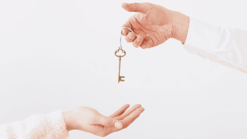 a hand holding a key on a chain with another hand below to accept it